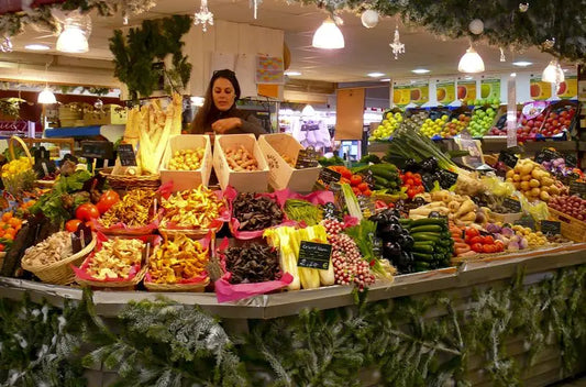 A vibrant market stall in Provence region, France, displaying a variety of fresh fruits and vegetables with a vendor attending to the display.